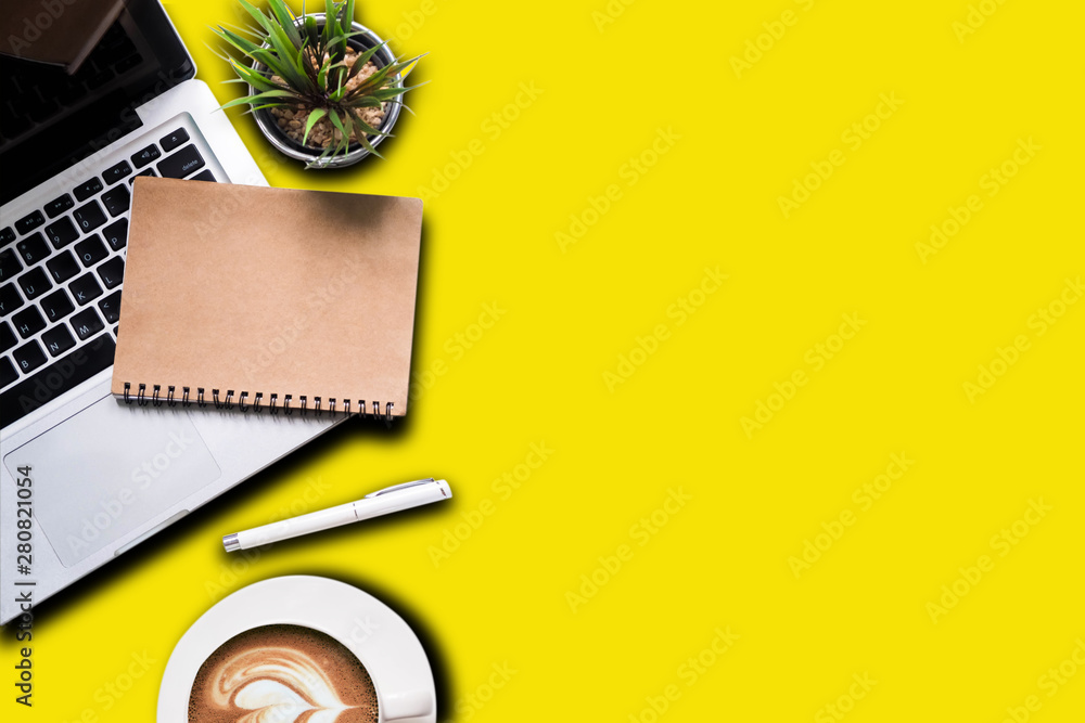 Office accessories laptop, smartphone, notepad, and coffee cup on a yellow table background. View from above. Office accessories laptop, smartphone, notepad, and coffee cup on a yellow table background. View from above.