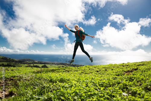 Portrait of fit positive girl jumping in the air on cloudy background with ocean view. Life people energy freedom concept. Sao Miguel island, Azores.