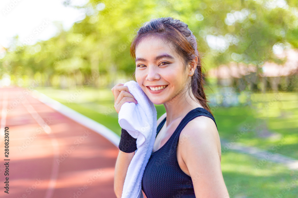 Beautiful young Asian woman wiping off her sweat after her morning exercise at a running track on a brtight sunny morning Beautiful young Asian woman wiping off her sweat after her morning exercise at a running track on a brtight sunny morning