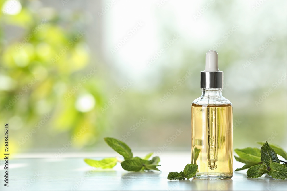 Bottle of mint essential oil on white wooden table against blurred background. Space for text Bottle of mint essential oil on white wooden table against blurred background. Space for text