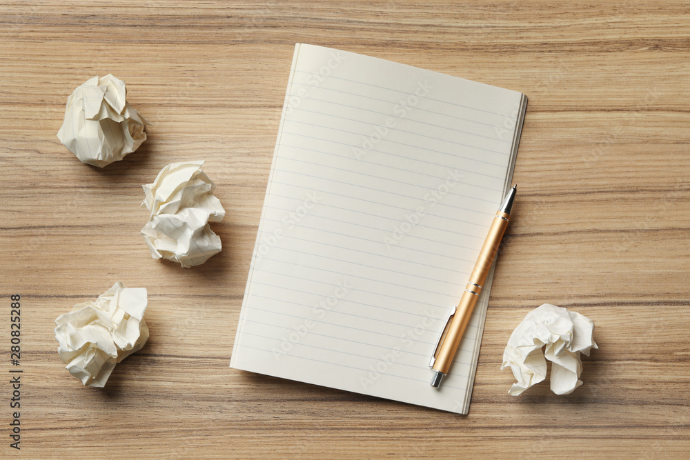 Fototapeta premium Empty notebook with pen and crumpled paper balls on wooden table, flat lay. Space for text