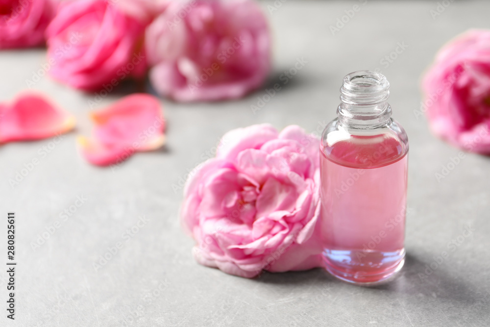 Bottle of rose essential oil and fresh flowers on table, space for text Bottle of rose essential oil and fresh flowers on table, space for text