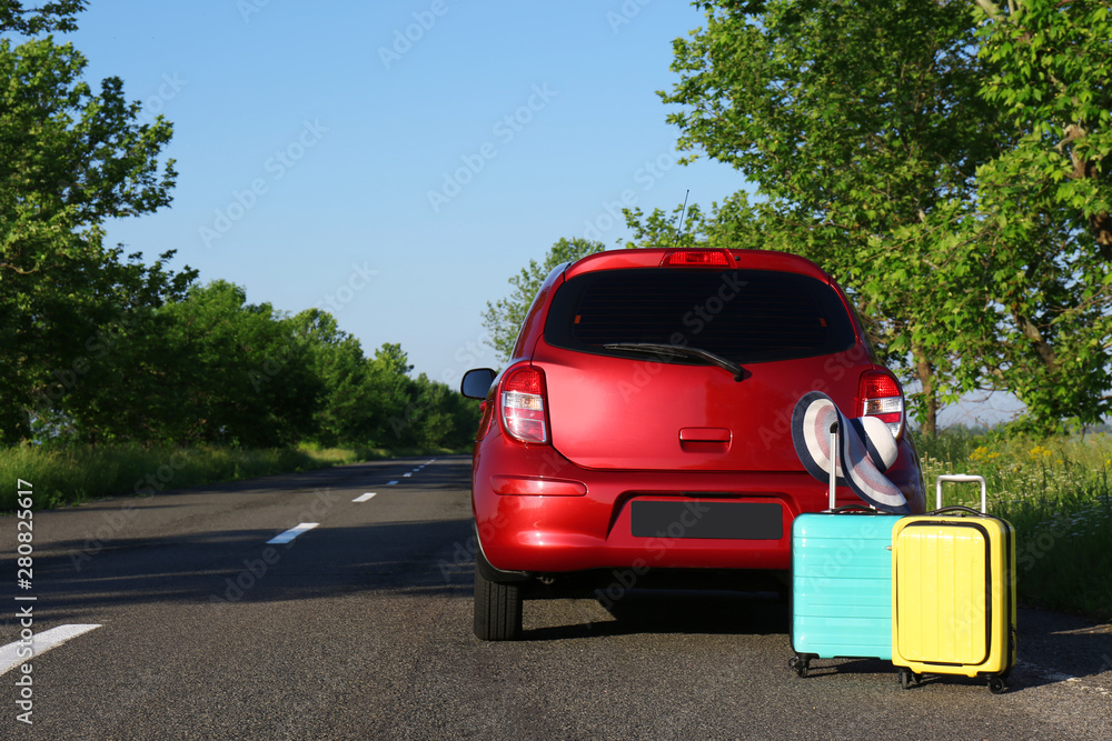 Color suitcases with hat near family car on highway. Space for text Color suitcases with hat near family car on highway. Space for text