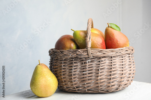 Ripe juicy pears in wicker basket on wooden table against light background