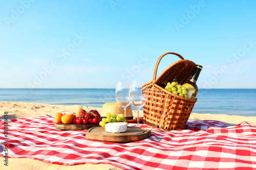 Checkered blanket with picnic basket and products on sunny beach photo