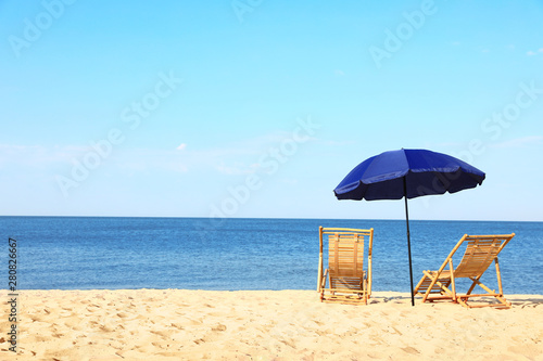 Empty wooden sunbeds and umbrella on sandy shore. Beach accessories © New Africa