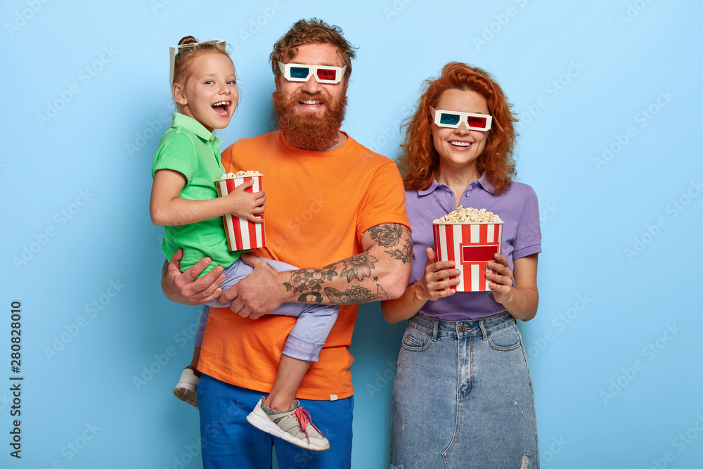 Φωτογραφία Optimistic three family members laugh happily, watch comedy in cinema together, enjoy eating delicious popcorn, express positive emotions, laugh at funny scene