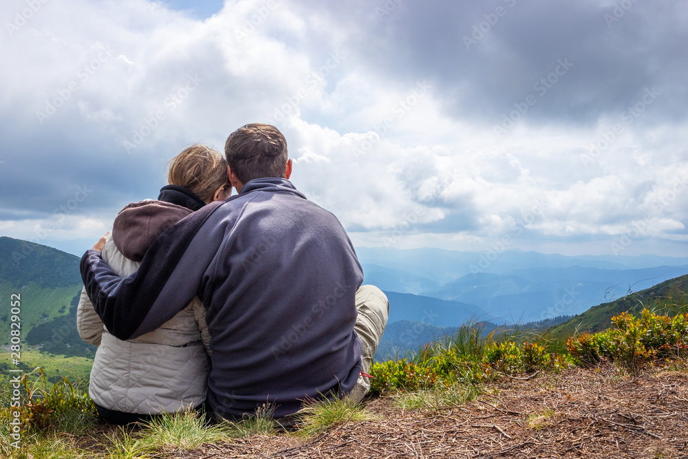 Happy couple of tourists during a travel in mountains, stand on the top and looking at the cloudy sky and the valley. Happy couple of tourists during a travel in mountains, stand on the top and looking at the cloudy sky and the valley.