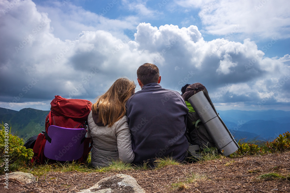 Happy couple of tourists during a travel in mountains, stand on the top and looking at the cloudy sky and the valley. Happy couple of tourists during a travel in mountains, stand on the top and looking at the cloudy sky and the valley.
