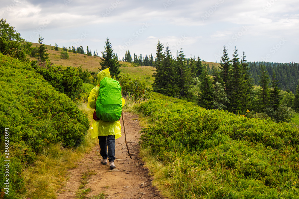 Hike backpacker lifestyle girl walking on trek trail in mountains outdoors with yellow raincoat and green raincover. Cold season gear hiking outside. Wanderlust and travel concept. Hike backpacker lifestyle girl walking on trek trail in mountains outdoors with yellow raincoat and green raincover. Cold season gear hiking outside. Wanderlust and travel concept.
