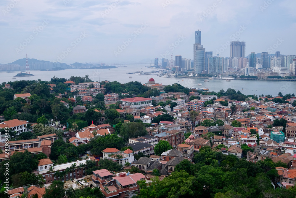 aerial view of Gulangyu(Kulangsu) Island. Dense red retro houses and trees. Modern skyscrapers on the other side of the river. Famous tourist city of China
