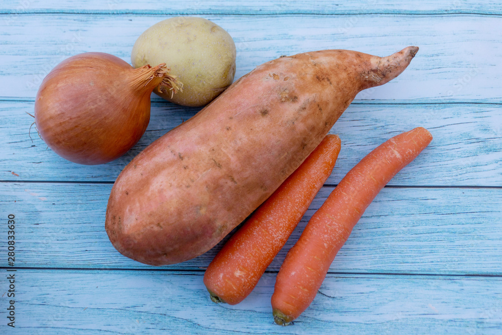Ripe carrots, potato, sweet potato and brown onion on a blue wooden table background. Cooking ingredients. Harvest Ripe carrots, potato, sweet potato and brown onion on a blue wooden table background. Cooking ingredients. Harvest