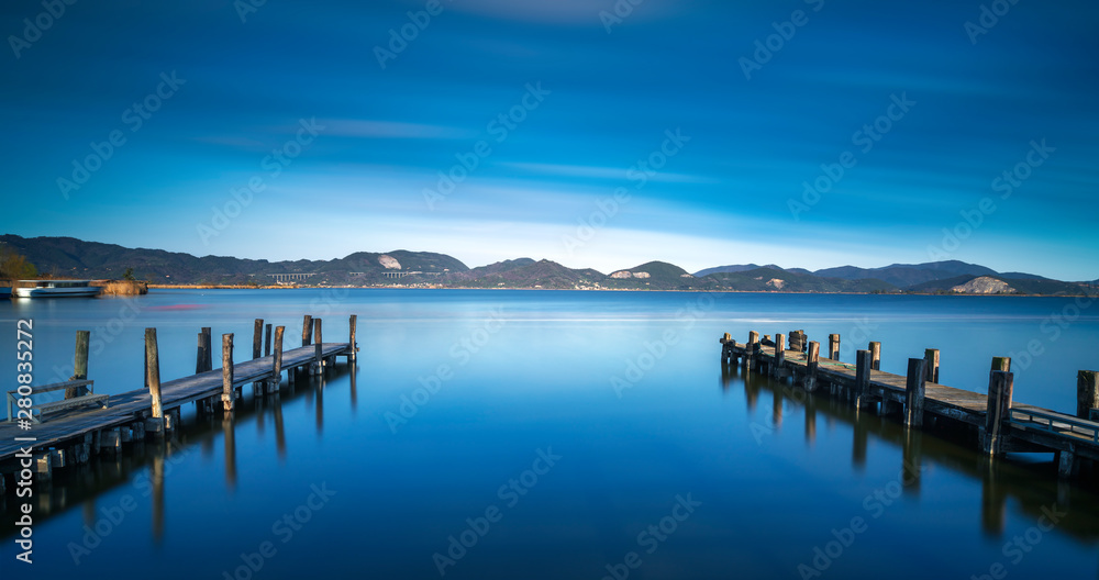 Two Wooden pier or jetty and on a blue lake sunset and sky reflection on water. Versilia Tuscany, Italy