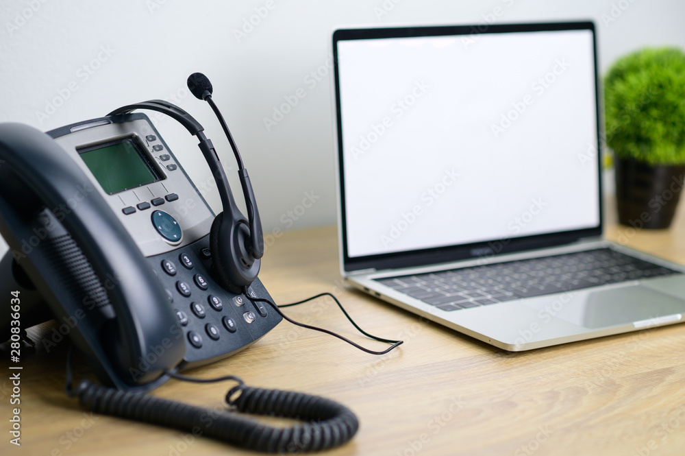 Office work space of IP Telephone with headset and laptop computer on wooden table Office work space of IP Telephone with headset and laptop computer on wooden table
