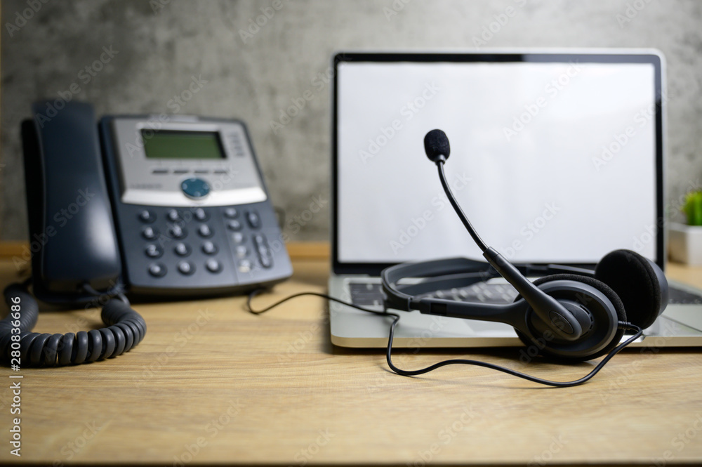 Headset on laptop computer and ip telephone on wooden table, office work space concept Headset on laptop computer and ip telephone on wooden table, office work space concept