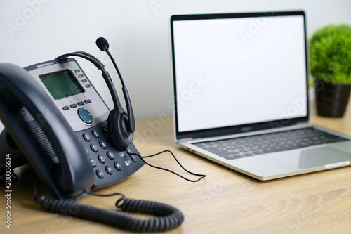 Office work space of IP Telephone with headset and laptop computer on wooden table