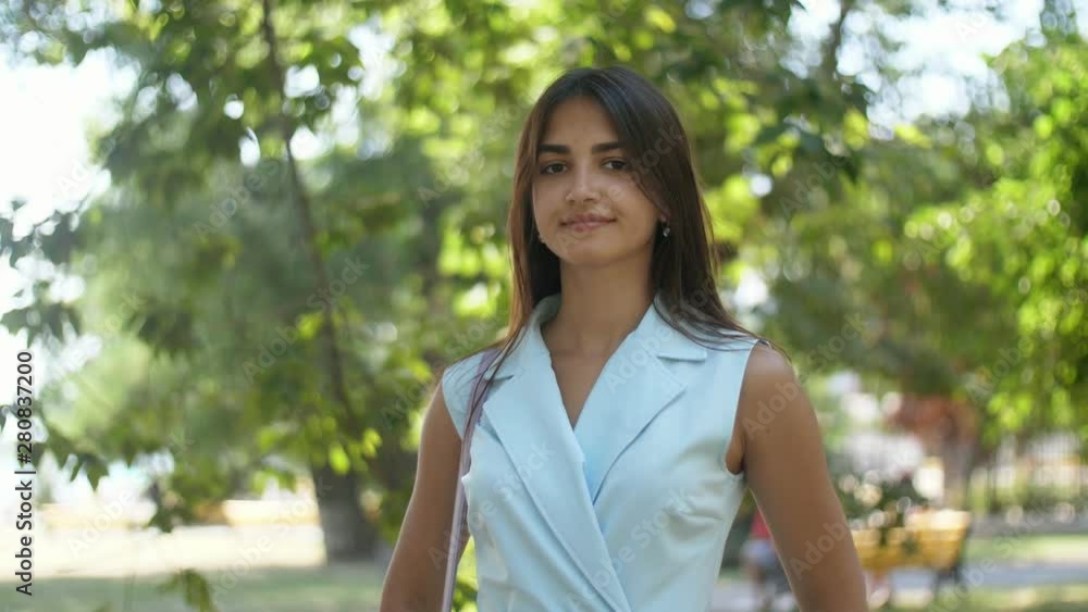 Elegant girl standing and smiling enigmatically in green park in summer in slo-mo Elegant girl standing and smiling enigmatically in green park in summer in slo-mo
