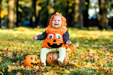 Cheerful little baby boy in halloween costume sitting on pumpkin, celebration