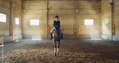 Cinematic slow motion close up of young female horsemanship master dressed in a professional apparel before practising exercises for competition of horse racing and dressage on a riding hall photo