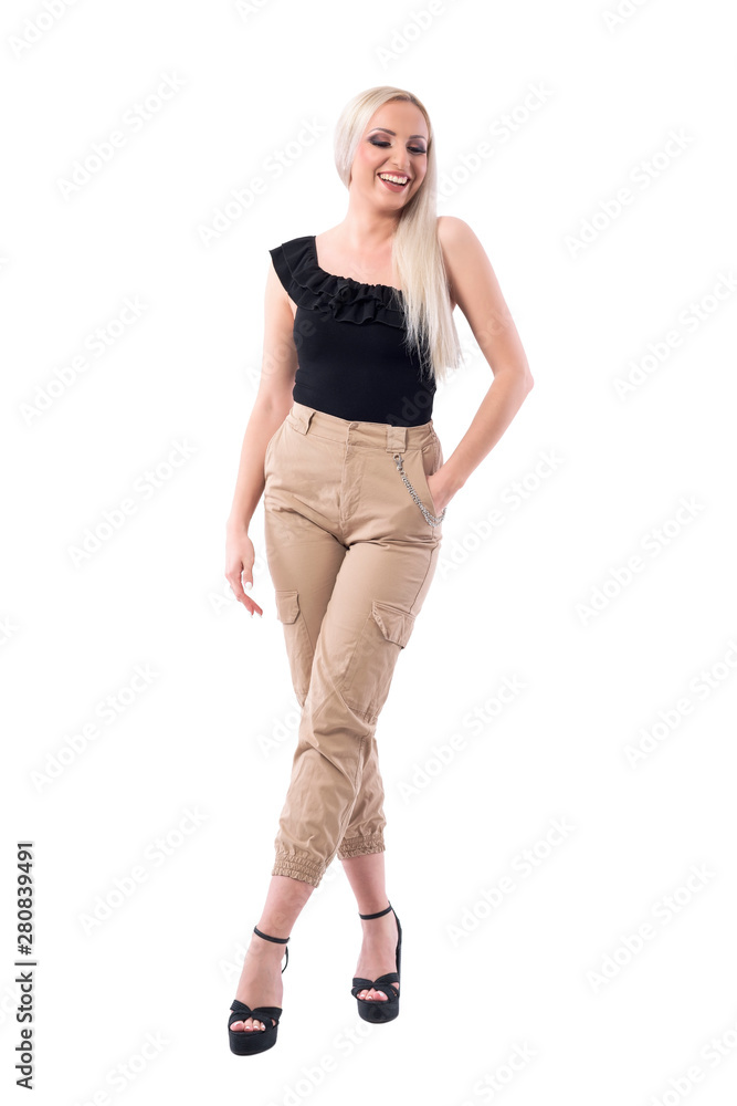 Stunning blonde glamorous woman laughing and looking down wearing cream color pants. Full body isolated on white background. Stunning blonde glamorous woman laughing and looking down wearing cream color pants. Full body isolated on white background.