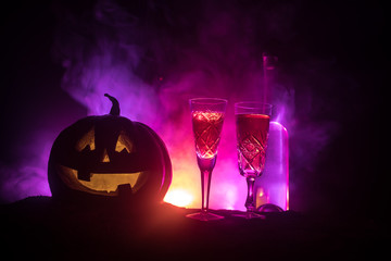 Two glasses of wine and bottle with Halloween - old jack-o-lantern on dark toned foggy background. Scary Halloween pumpkin