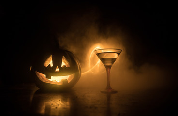 Halloween pumpkin orange cocktails. Festive drink. Halloween party. Funny Pumpkin with a glowing cocktail glass on a dark toned foggy background.