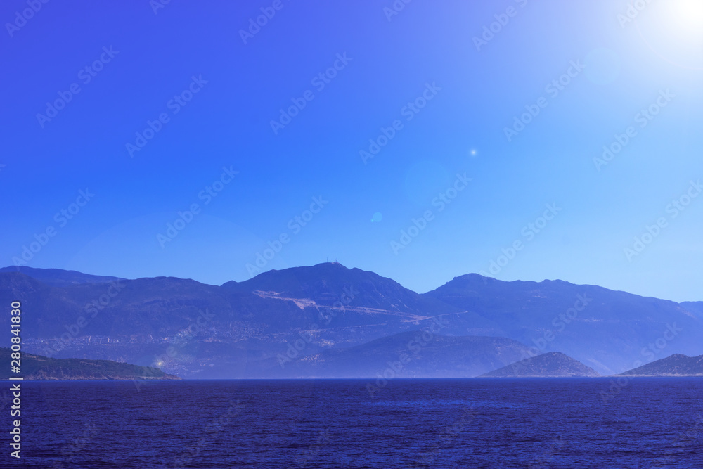 Creative layout made of seascape with mountains in fog and bright sunbeams, touristic season. Mediterranian calm sea.