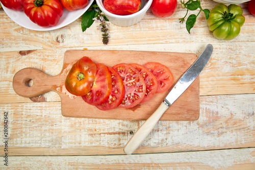 Chopped tomatoes and knife on cutting board. Mix of tomatoes background. Beautiful juicy organic red tomatoes on white wooden table background. Clean eating concept. Copy space, flat lay.