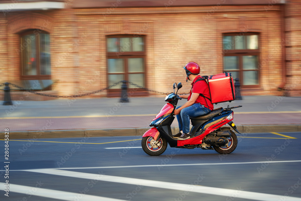 Delivery boy of takeaway on scooter with isothermal food case box driving  fast. Express food delivery service from cafes and restaurants. Courier on  the moto scooter delivering food. foto de Stock