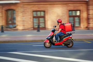 Delivery boy of takeaway on scooter with isothermal food case box driving fast. Express food delivery service from cafes and restaurants. Courier on the moto scooter delivering food.