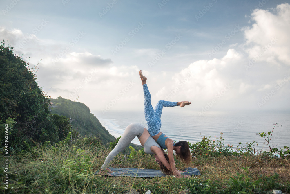 Pair of girls practice yoga against the background of the ocean Pair of girls practice yoga against the background of the ocean