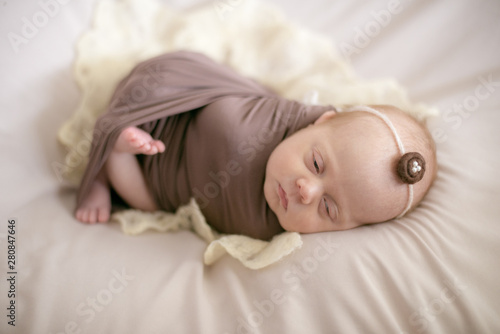 sleeping newborn baby in a wrap brown blanket on the bed