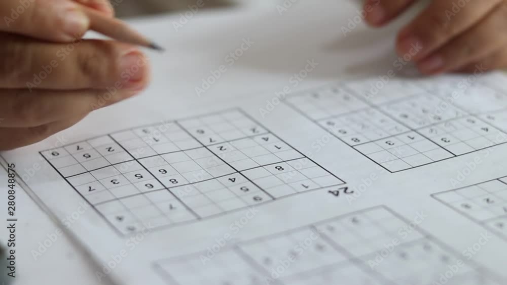 Solve sudoku puzzle with pencil as hobby by senior woman on wooden office desk. Player insert numbers into grid consisting of nine squares subdivided into further nine smaller squares. Solve sudoku puzzle with pencil as hobby by senior woman on wooden office desk. Player insert numbers into grid consisting of nine squares subdivided into further nine smaller squares.