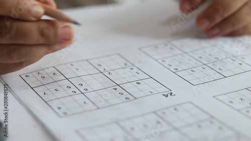 Solve sudoku puzzle with pencil as hobby by senior woman on wooden office desk. Player insert numbers into grid consisting of nine squares subdivided into further nine smaller squares. photo