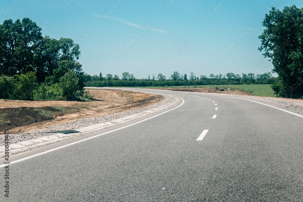 Fototapeta premium New asphalt road with roadside construction site in the forest. Countryside asphalt road reconstruction