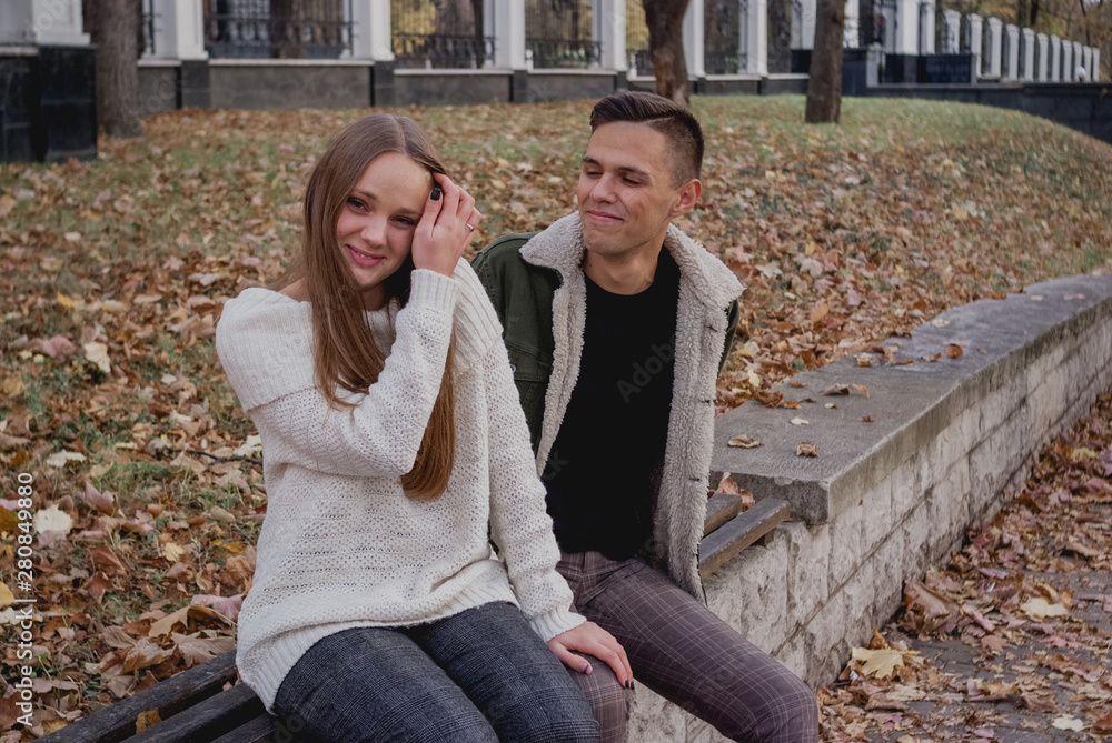 Couple in love stand on autumn fallen leaves in a park, enjoying a beautiful autumn day. Man hugs girl Couple in love stand on autumn fallen leaves in a park, enjoying a beautiful autumn day. Man hugs girl