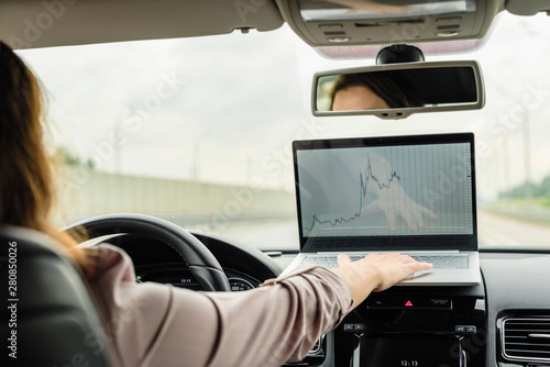 Business woman turn on car emergency stop button driving on the highway and working using laptop.