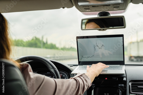 Business woman turn on car emergency stop button driving on the highway and working using laptop.