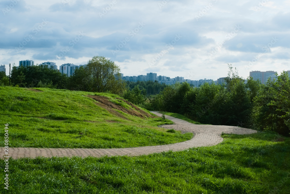 Beautiful landscape with green grass and modern buildings. The path is hidden behind the hill.