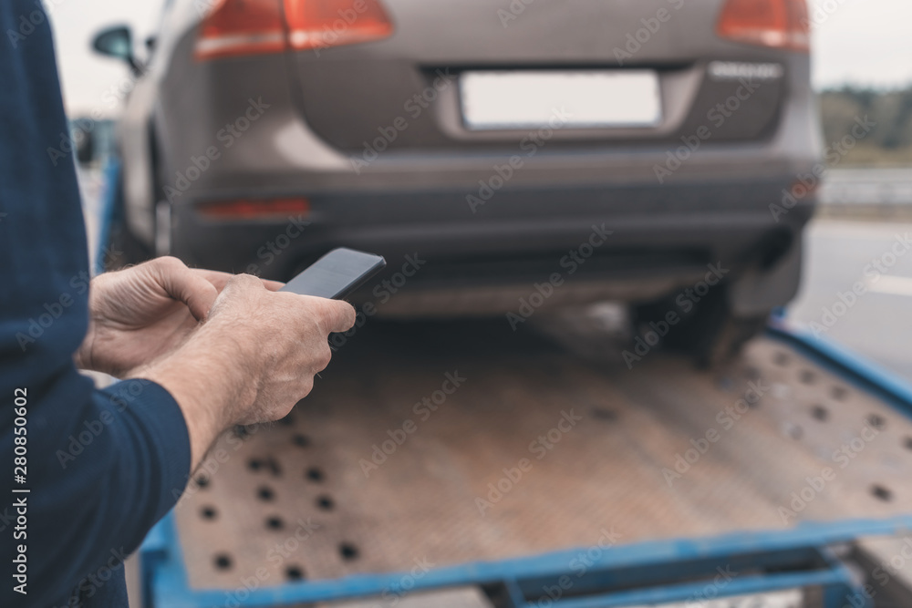 Man with mobile phone.Tow truck with worker towing a broken down car on the highway. Selective focus. Concept Man with mobile phone.Tow truck with worker towing a broken down car on the highway. Selective focus. Concept