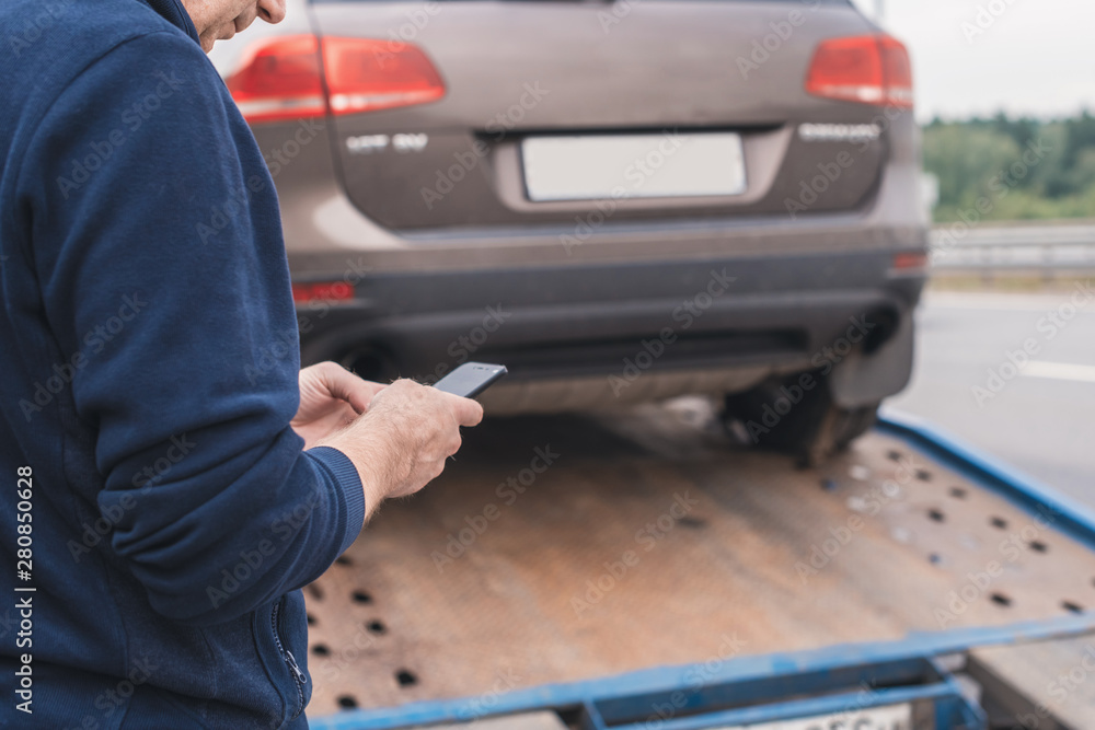 Man with mobile phone.Tow truck with worker towing a broken down car on the highway. Selective focus. Concept Man with mobile phone.Tow truck with worker towing a broken down car on the highway. Selective focus. Concept