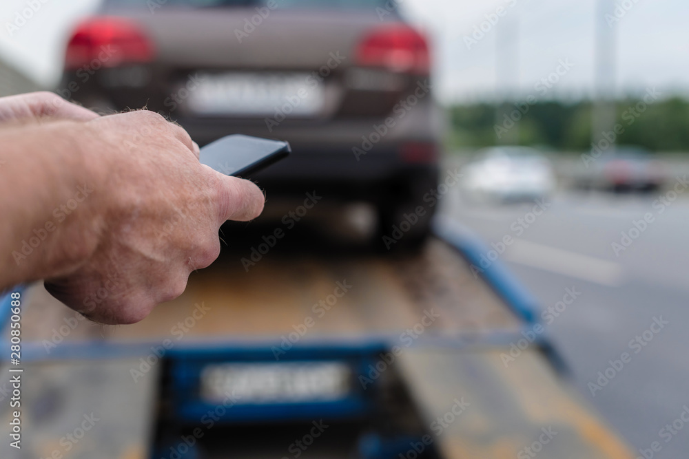 Naklejka premium Man with mobile phone.Tow truck with worker towing a broken down car on the highway. Selective focus. Concept