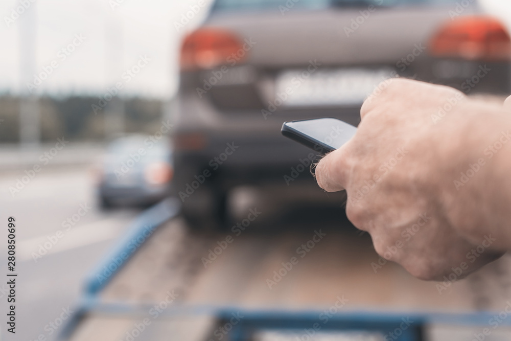 Man with mobile phone.Tow truck with worker towing a broken down car on the highway. Selective focus. Concept Man with mobile phone.Tow truck with worker towing a broken down car on the highway. Selective focus. Concept