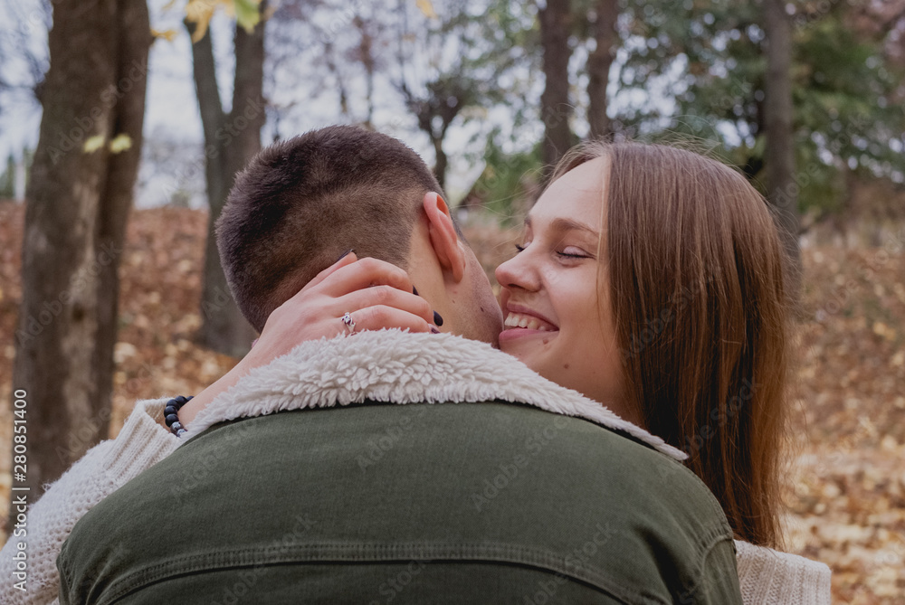 Fototapeta premium Couple in love stand on autumn fallen leaves in a park, enjoying a beautiful autumn day. Man hugs girl