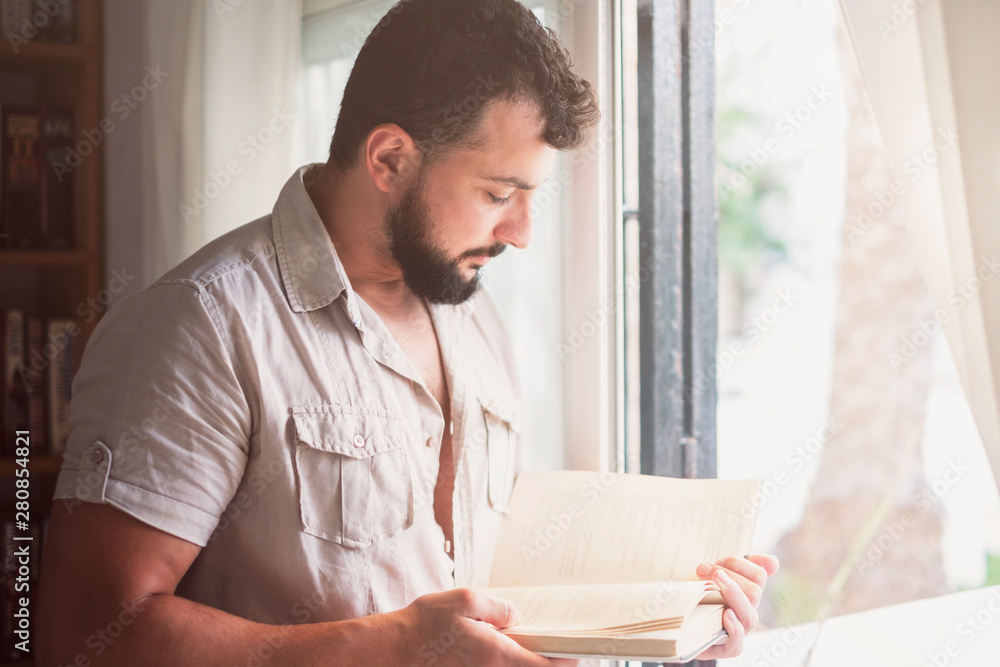 Fototapeta premium bearded man reading book near to window