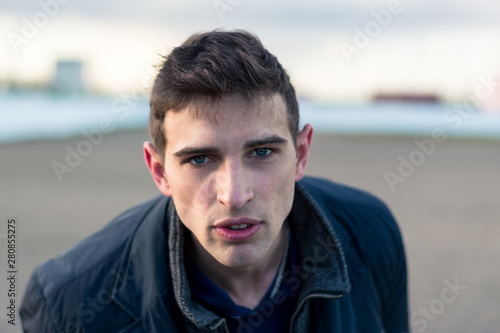 dramatic portrait of a young, brutal-looking man. Close-up. Fashionable hairstyle and manly bristles. Wearing a black leather jacket. A facial expression sends a message. on the background of a little