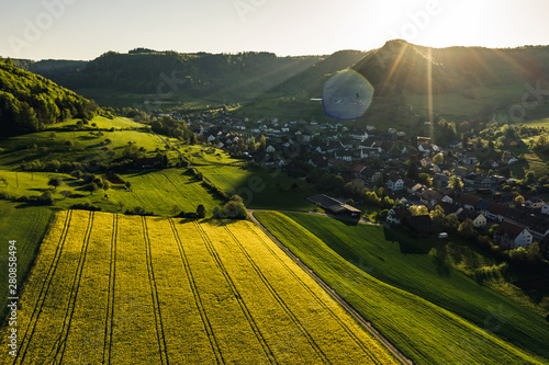 aerial overview of countryside during golden hour with yellow flowers in a small village, Field of rapeseed in full flower, spring time in countryside switzerland
