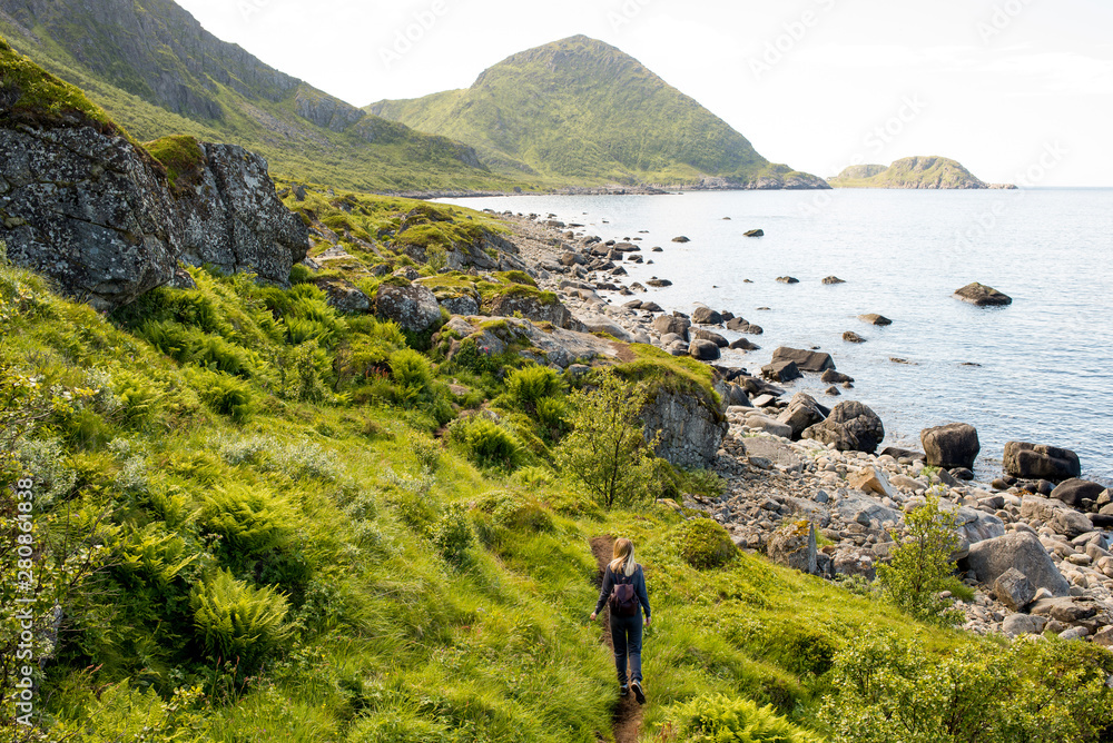 Woman goes on tourist hiking trail along ocean and mountains in Norway. Active recreation, healthy lifestyle. Enjoys scenic view. Beautiful nature. Travel, adventure. Sense of freedom. Explore North