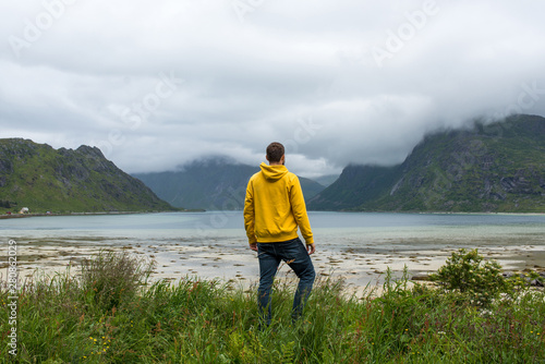 Men in yellow hoodie outdoor enjoys the scenic view of the fjord. Stunning beauty nature. Harmony, relax lifestyle. Travel, adventure. Sense of freedom. Explore North Norway. Summer in Scandinavia