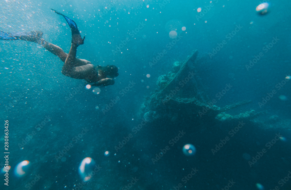 Obraz premium Discovering a japanese ship wreck from second world war. Beautiful woman swimming underwater in a tropical sea. under water shot with action camera. concept about wanderlust travels